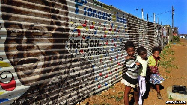 Children pose as they stand next to a mural of former South African President Nelson Mandela and other freedom fighters in the Orlando District of Soweto on 30 June 2013 in Johannesburg, South Africa