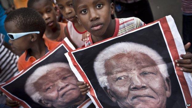 South African children hold placards showing the face of Nelson Mandela as they celebrate his life, in the street outside his old house in Soweto, Johannesburg, South Africa - Friday 6 December 2013