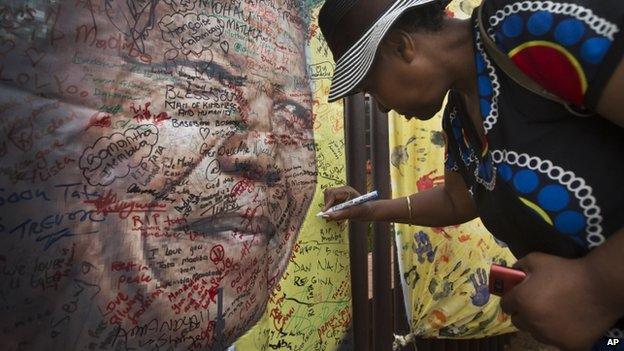 A well-wisher writes a message on a poster of Nelson Mandela on which she and others have written their messages of condolence and support, in the street outside his old house in Soweto, Johannesburg, South Africa Friday, 6 December 2013