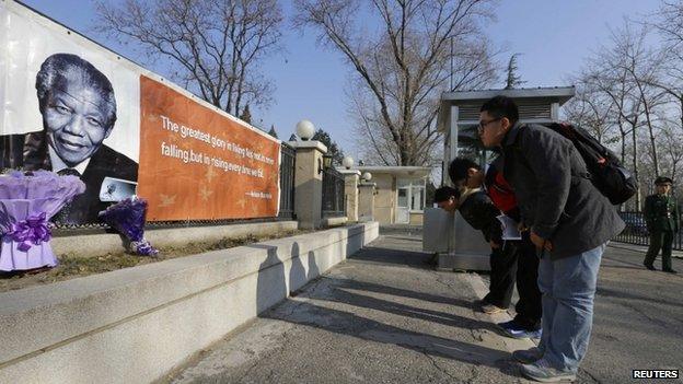 Chinese residents bow to a banner bearing a picture of former South African President Mandela as they pay tribute in front of the South African Embassy in Beijing