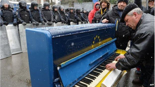 A man plays on a piano decorated with EU flag in front of riot police outside the presidential office