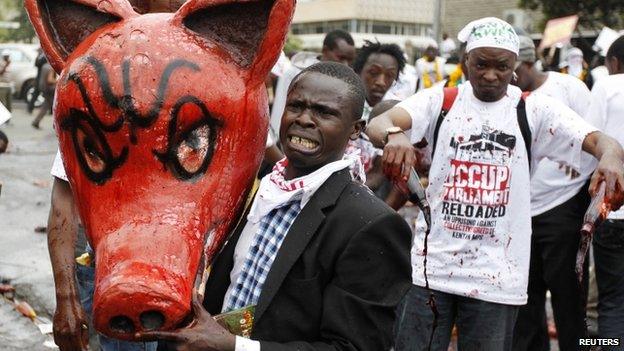 A protester carries a dummy pig head covered with animal blood, reacts as he participates in a demonstration against lawmakers" demands for a pay rise