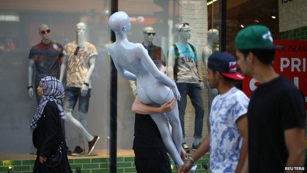 Shoppers pass a man carrying a shop window mannequin as he moves items to new premises on Oxford Street in London