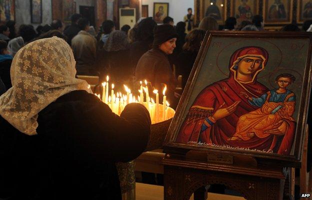 A Syrian woman lights candles as she attends early Christmas eve mass, at the Mar Elias (St. Elijah) Christian Orthodox church in Bab Tuma