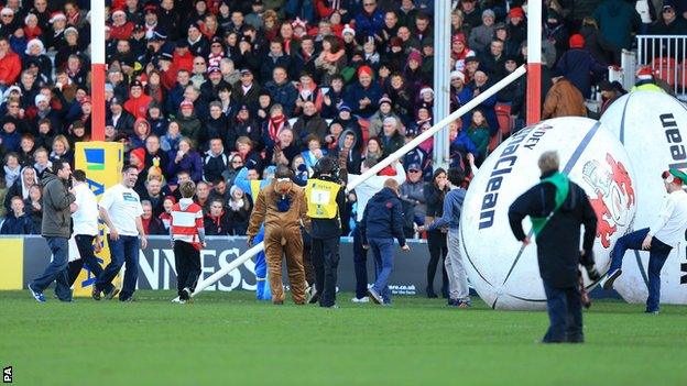 Officials survey the damage after a giant rugby ball knocks off the crossbar before kick-off