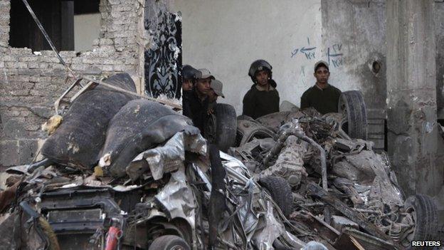 Police officers stand near damaged vehicles outside the building of Directorate of Security