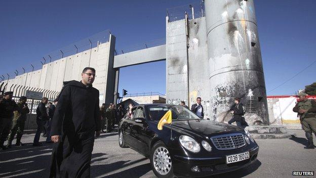 The Latin Patriarch of Jerusalem waves from a car as he is driven through an Israeli checkpoint into Bethlehem to attend Christmas celebrations