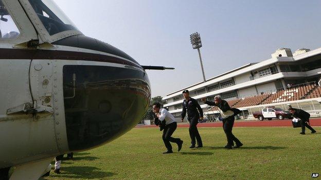 Thai election commission officials are escorted by a policeman to a helicopter during an evacuation after the registration was disrupted by anti-government protesters at a sport stadium in Bangkok