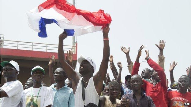 A Malian man holds a French flag and cheers as he listens to the French President make a speech during the inauguration celebration of Mali's new president at the March 26 stadium in Bamako, sept 2013