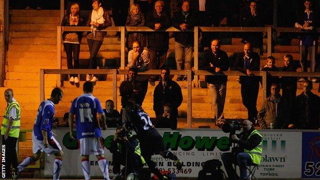 Supporters stand at a match at Brunton Park