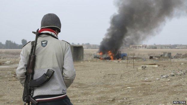 Iraqi militant looks at burning police vehicle in Ramadi (2 January 2014)