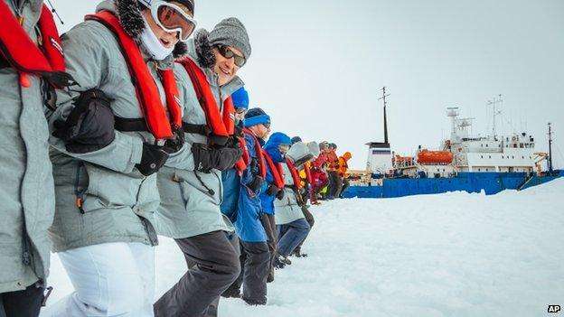 Passengers from the Russian ship MV Akademik Shokalskiy link arms and stamp out a helicopter landing site on the ice