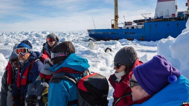 Penguins and passengers from the stranded Russian ship Akademik Shokalskiy wait for a helicopter from the nearby Chinese icebreaker Xue Long to pick them up after over a week of being trapped in the ice off Antarctica