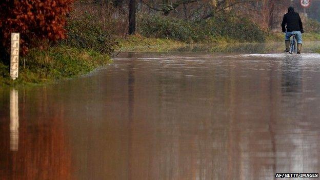 A man rides his bicycle through flood water in the village of Queen Street in Kent, southern England