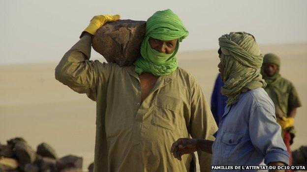 man in colourful headscarf carries a rock on his shoulder