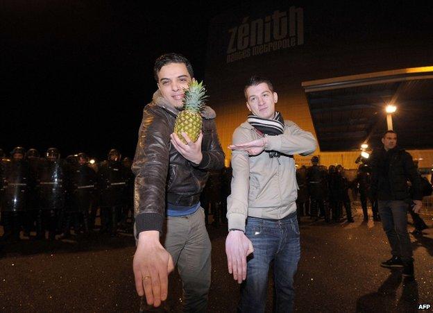 One man holds a pineapple while he and another makes quenelle salutes outside the Zenith concert hall in Nantes, 9 January