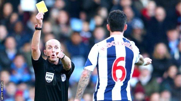 Referee Mike Dean cautions Liam Ridgewell