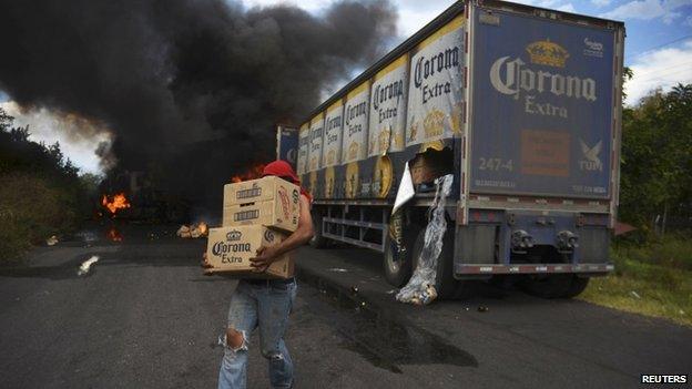 A looter carries boxes of beer as Corona truck burns in a road block allegedly set up by followers of the Knights Templar cartel in Tierra Caliente on 10 January, 2014