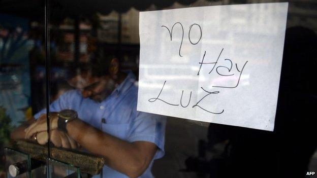 An employee of a business closed during a blackout stands behind the door with a notice reading "There's no electricity" in Caracas on 3 September, 2013