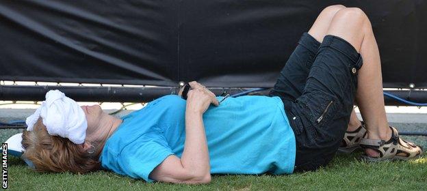 A tennis fan seeks the shade as temperatures remain high