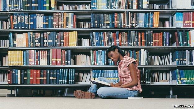 A student sitting on the floor at a library reading a book