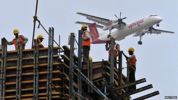 Construction workers erect scaffolding at the site of a metro station as a SpiceJet Airlines aircraft flies past in the southern Indian city of Chennai