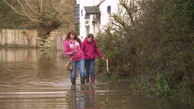 Residents wade through water surrounding a house