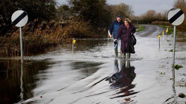 A couple approach flood water on the road at Burrow Bridge, Somerset