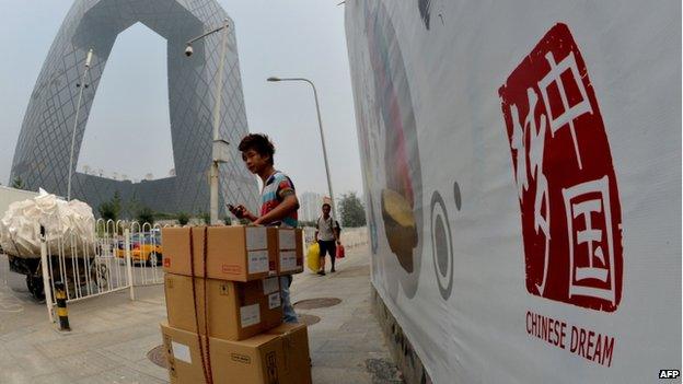 A Chinese migrant worker stands beside a "Chinese Dream" poster