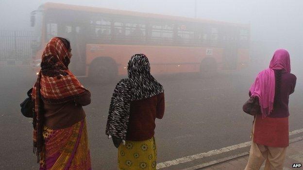 Indian commuters wait for a bus early on a polluted morning in New Delhi