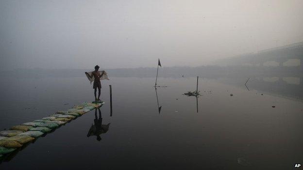 A man uses a cloth to dry himself after taking a dip in the polluted waters of the Yamuna River on a winter morning in New Delhi