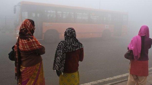 Indian commuters wait for a bus early on a polluted morning in New Delhi