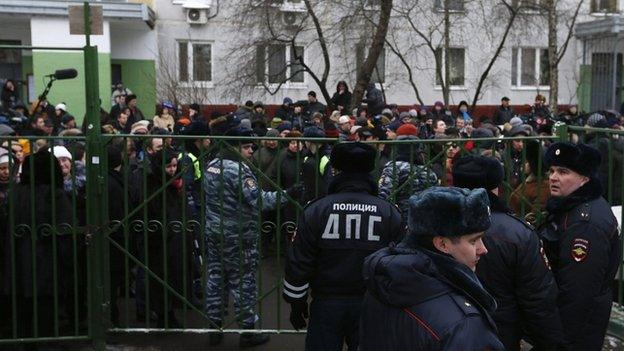 Bystanders and relatives of students gather behind a fence near the school