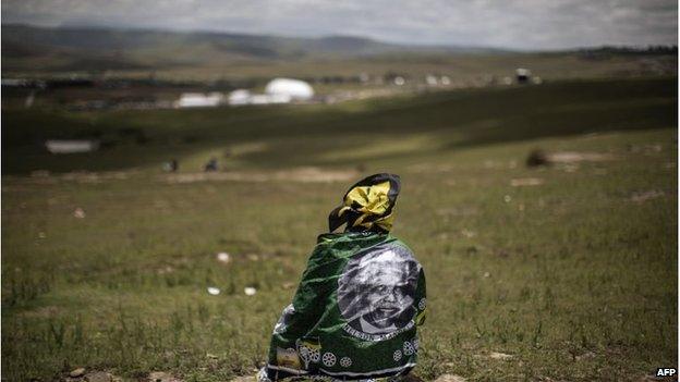 A woman looks on as South African former president Nelson Mandela's coffin is carried to his burial site during his state funeral in his home village in Qunu. Qunu's high school will receive 100,000 rand from his will.