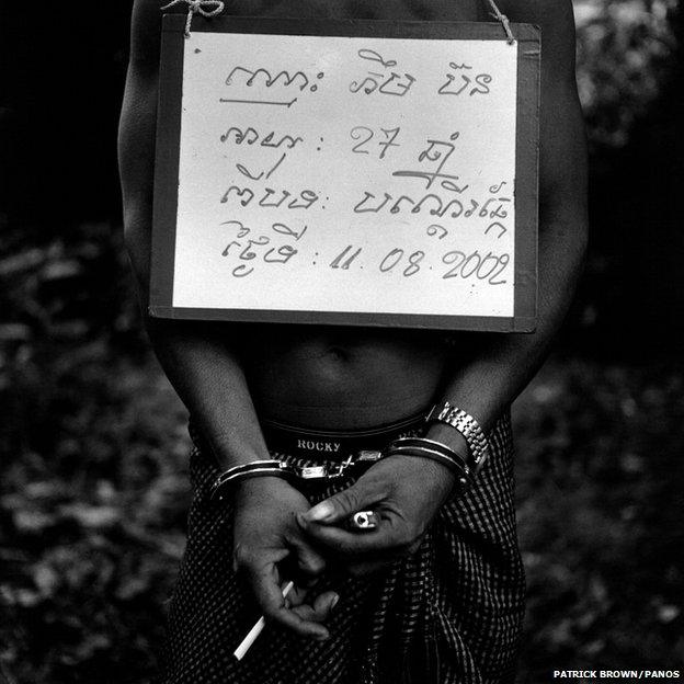 A handcuffed poacher is photographed with a notice bearing details of his name, age and the nature and date of his crime