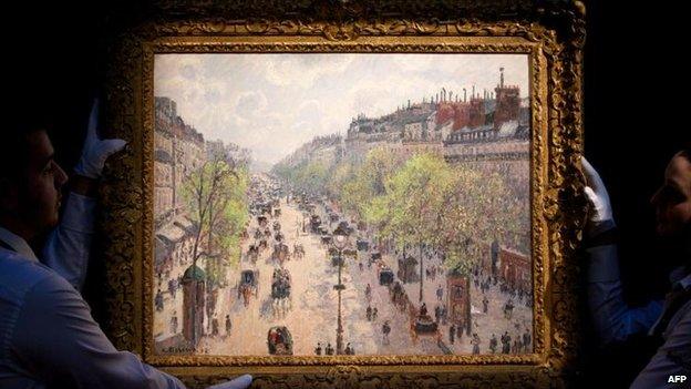 Sotheby's employees hold up Camille Pissarro's Le Boulevard Montmartre, matinee de printemps (1897)