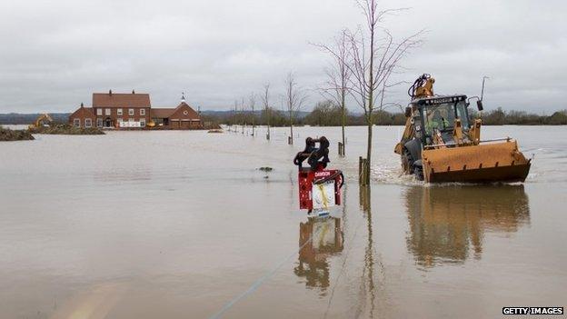 A mechanical digger is driven through floodwater in the village of Moorland