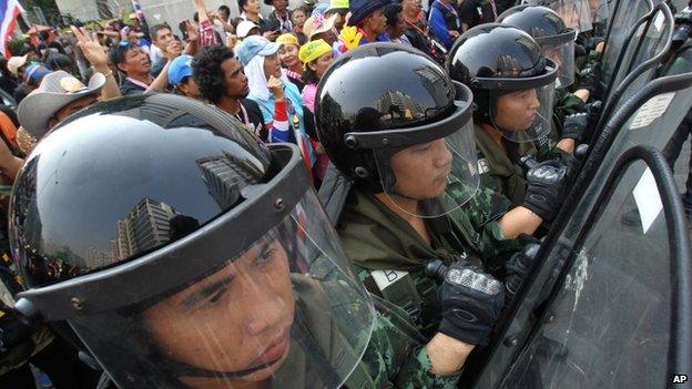 Thai soldiers stand guard to block anti-government protesters, left, during a rally outside the office of the permanent secretary for defence where Prime Minister Yingluck Shinawatra was reportedly working on 3 February 2014