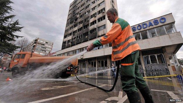 Worker cleans road in front of burned government building in Tuzla on 8 February 2014