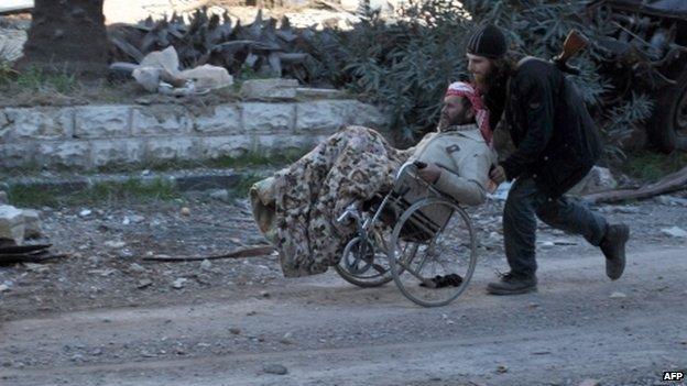 A civilian in a wheelchair is aided by an armed man ahead of being evacuated by the UN from a besieged district of Homs