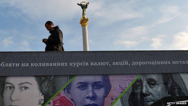 A man stands next to an advertising placard showing British pounds, US dollars and Ukrainian hryvnia banknotes on a warm autumn day in the Ukrainian capital Kiev on 12 November 2012.