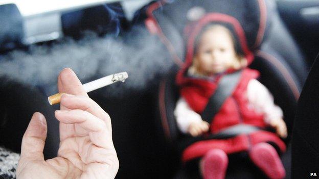 Person smoking in car with a small child in the back seat