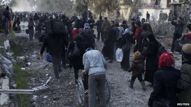 Civilians walk towards a meeting point to be evacuated from a besieged area of Homs on 10 February 2014