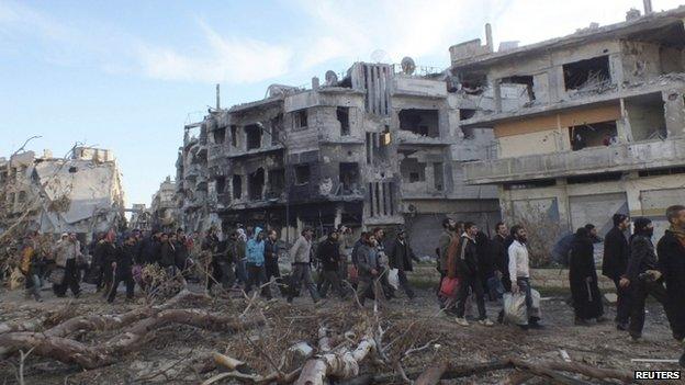 Civilians carry their belongings as they walk towards a meeting point to be evacuated from a besieged area of Homs on 10 February 2014