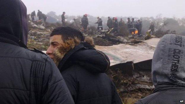 People watch rescue workers working at the wreckage of an Algerian military transport aircraft after it slammed into a mountain in the country's rugged eastern region