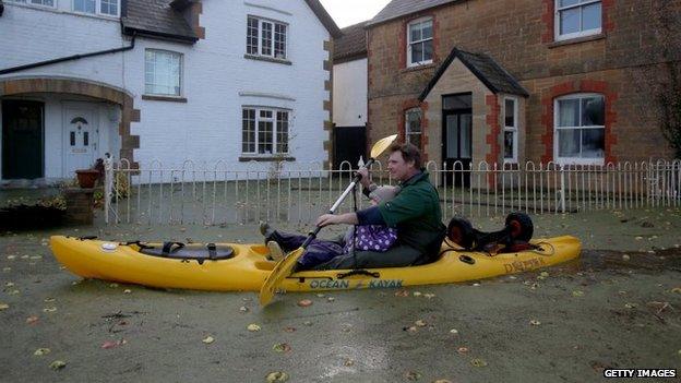 A resident uses a canoe on flood water past houses on the road leading to Muchelney