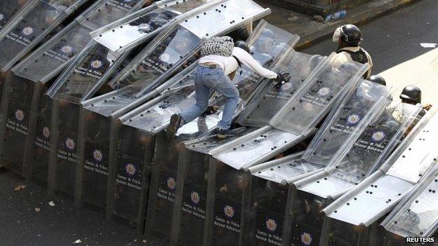 A demonstrator jumps on shield wall formed by riot police during a protest against the government in Caracas on 12 February, 2014