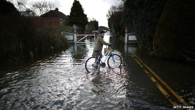 A resident pushes her bike through flood water in Staines-Upon-Thames