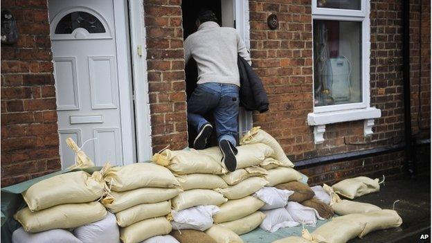 A man climbs over a high pile of sandbags to get into the front door of a house