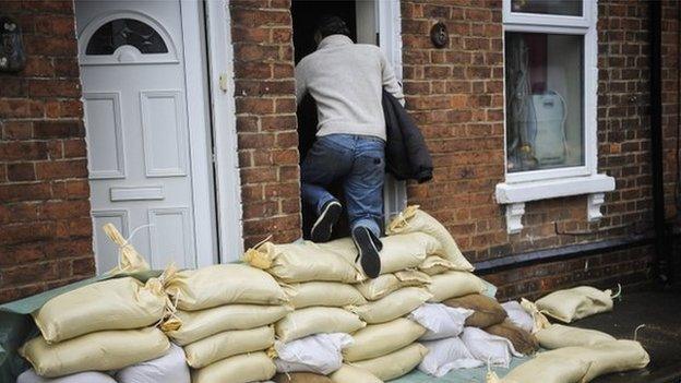 A man climbs over a high pile of sandbags to get into the front door of a house